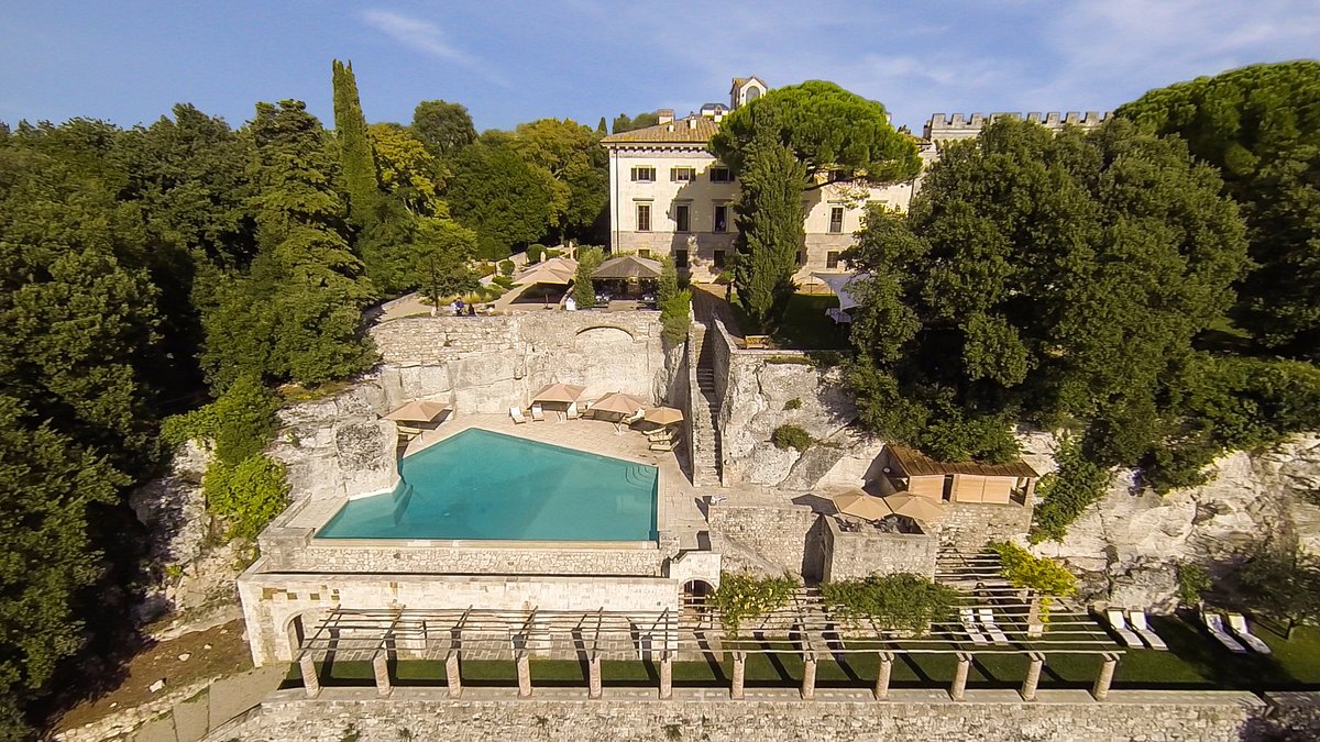 Aerial view of Borgo Pignano in Tuscany. Rustic brick hotel and large pool surrounded by trees. 