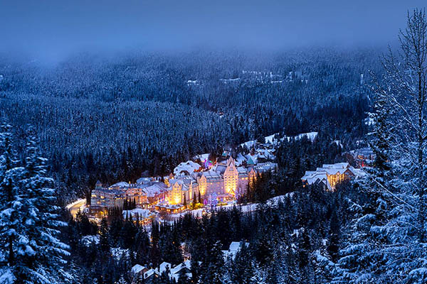 Fairmont Chateau Whistler lighted up and surrounded by pine trees covered in snow. 